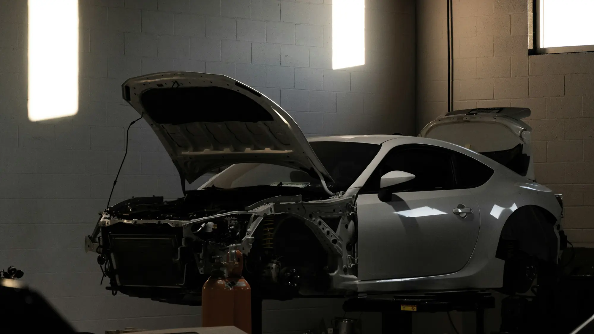 Stripped car bodyshell standing under work lights in a dark repair bay
