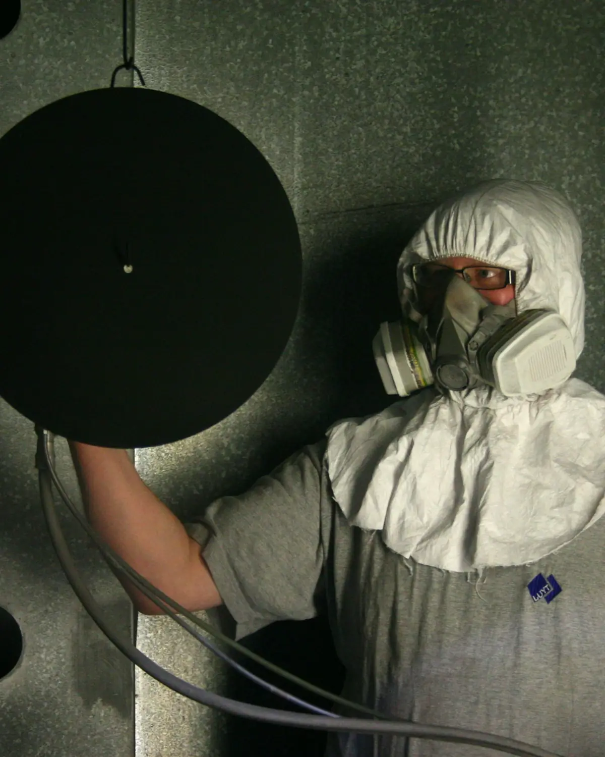 Spray painter in a full suit and respirator holding a sanding disc