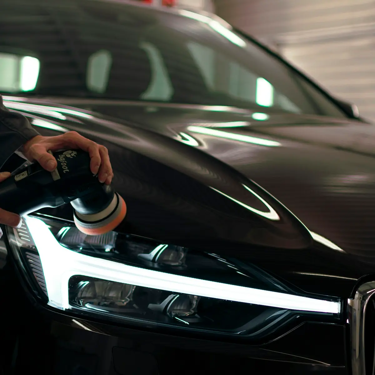 Machine polisher cutting the clearcoat on a dark car bonnet