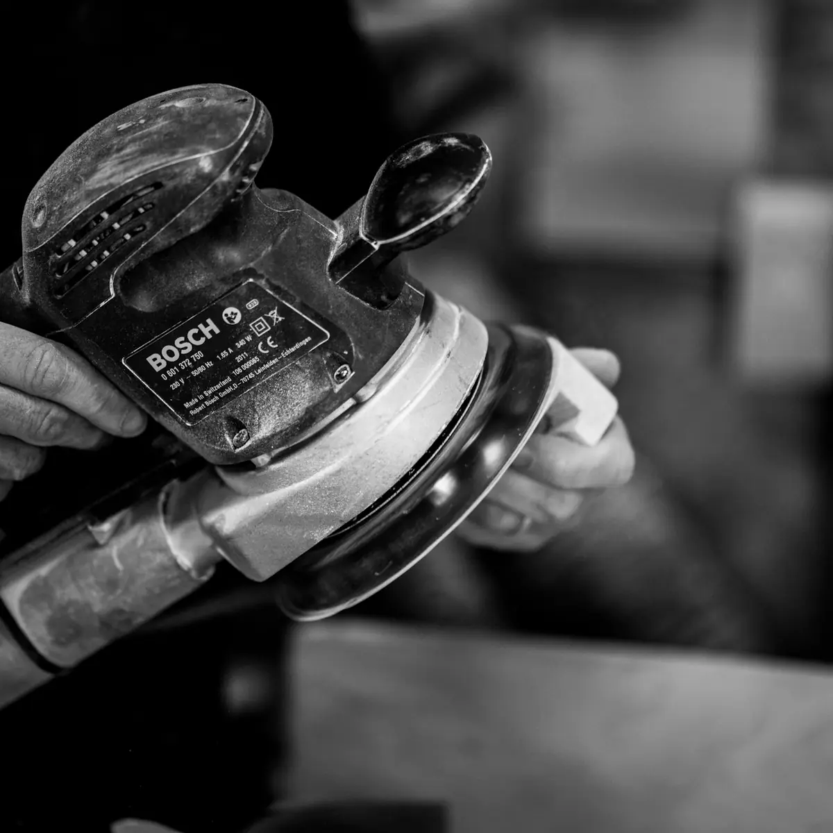 Hands gripping a dual action sander over bare metal